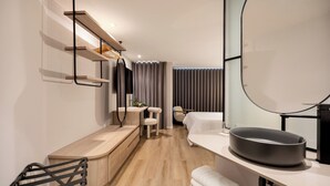 Una habitación de hotel moderna con un escritorio integrado, un espejo grande, una mesa redonda negra y una zona de estar con una silla y un banco.