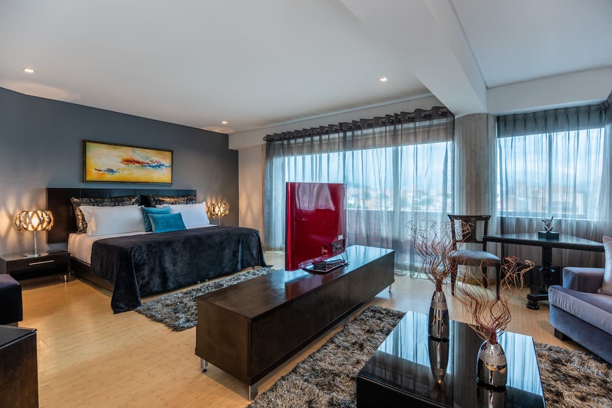Un dormitorio moderno con una cama grande, un televisor de pantalla plana y vistas a la ciudad a través de cortinas translúcidas.