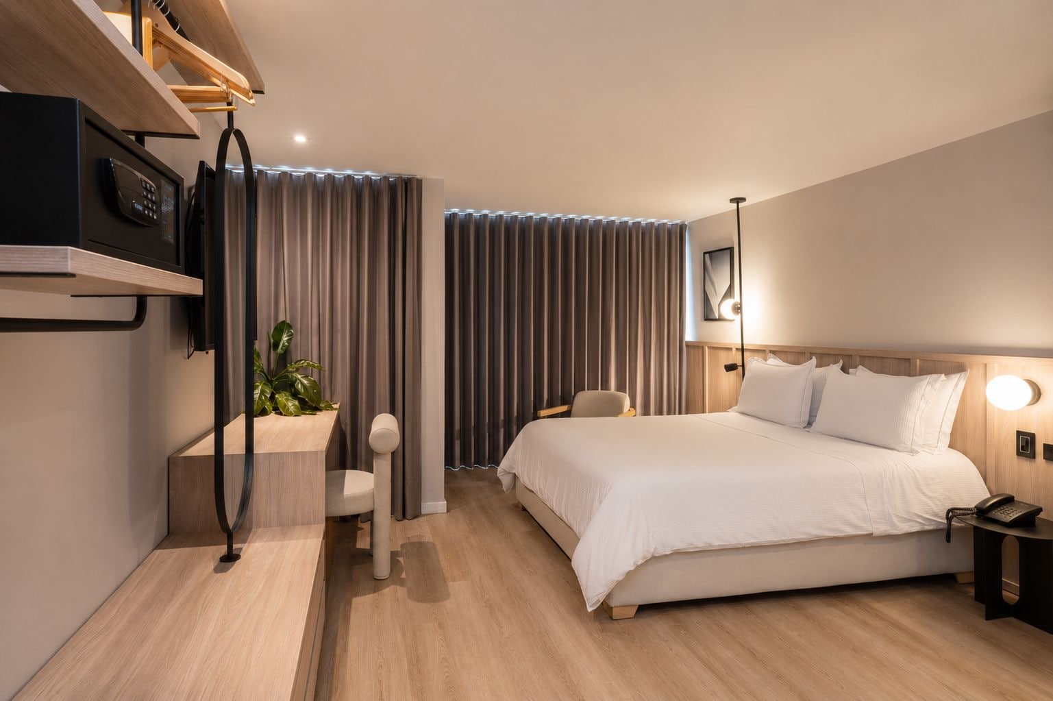 A modern hotel room with a bed, bedside table, lamp, and a small desk with a chair.