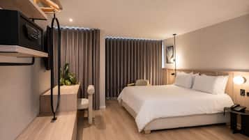 A modern hotel room with a bed, bedside table, lamp, and a small desk with a chair.