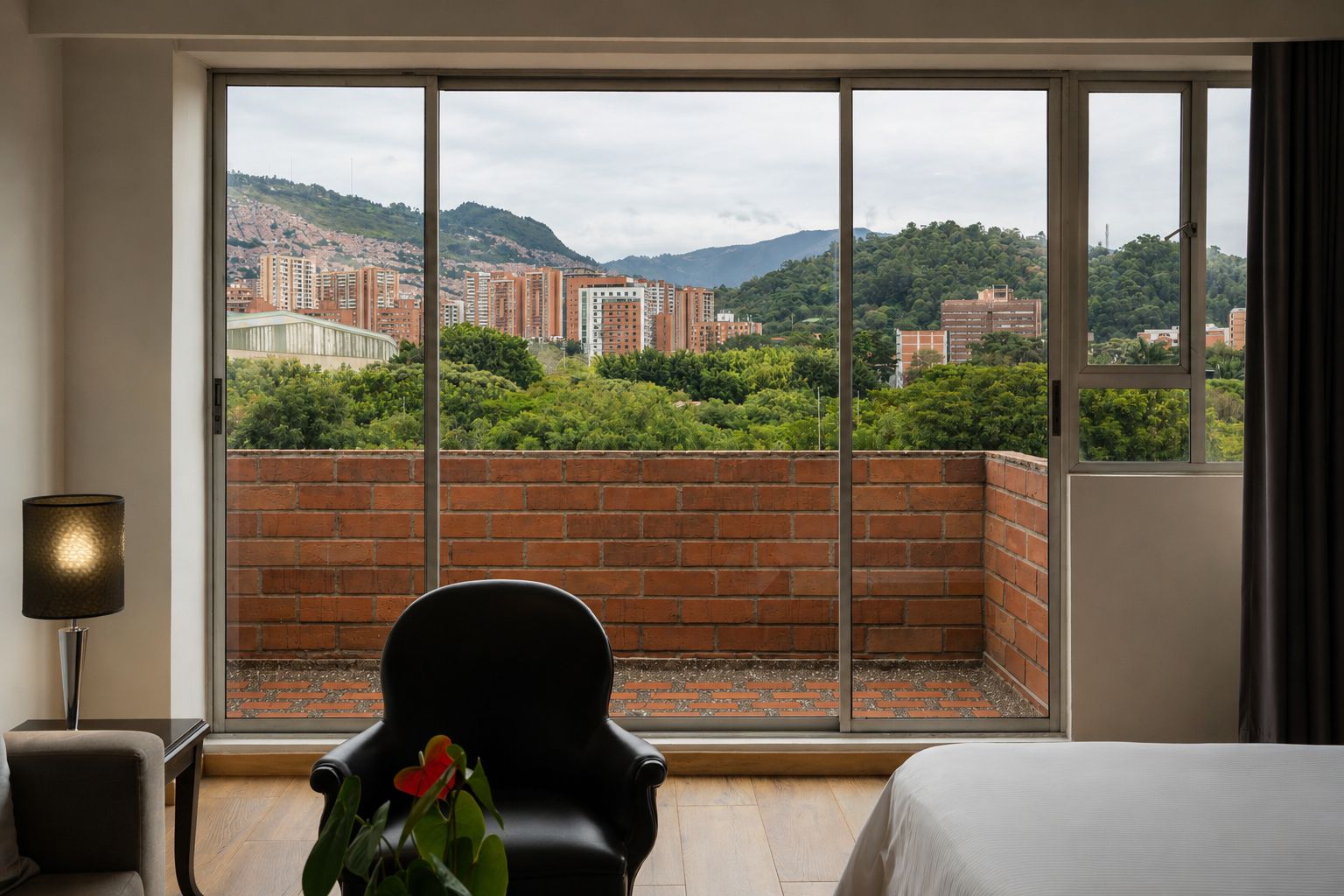 A hotel room with a large window, a chair, a bed, and a lamp.