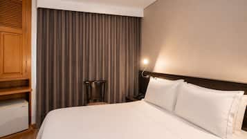 A hotel room with a bed, a wooden cabinet, a chair, and a curtain.