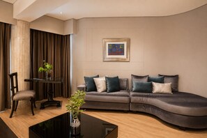 Una sala moderna con un sofá curvo, una mesa de centro de vidrio y una obra de arte enmarcada en la pared.
