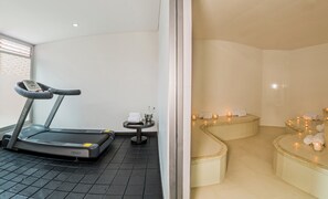 A gym with a treadmill, a small table with a bottle and a towel, and a spa area with candles and towels. - Hotel Egina Medellín (Medellín)
