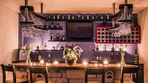 Zona de bar con pared de ladrillo, televisión de pantalla plana y una variedad de botellas y vasos.