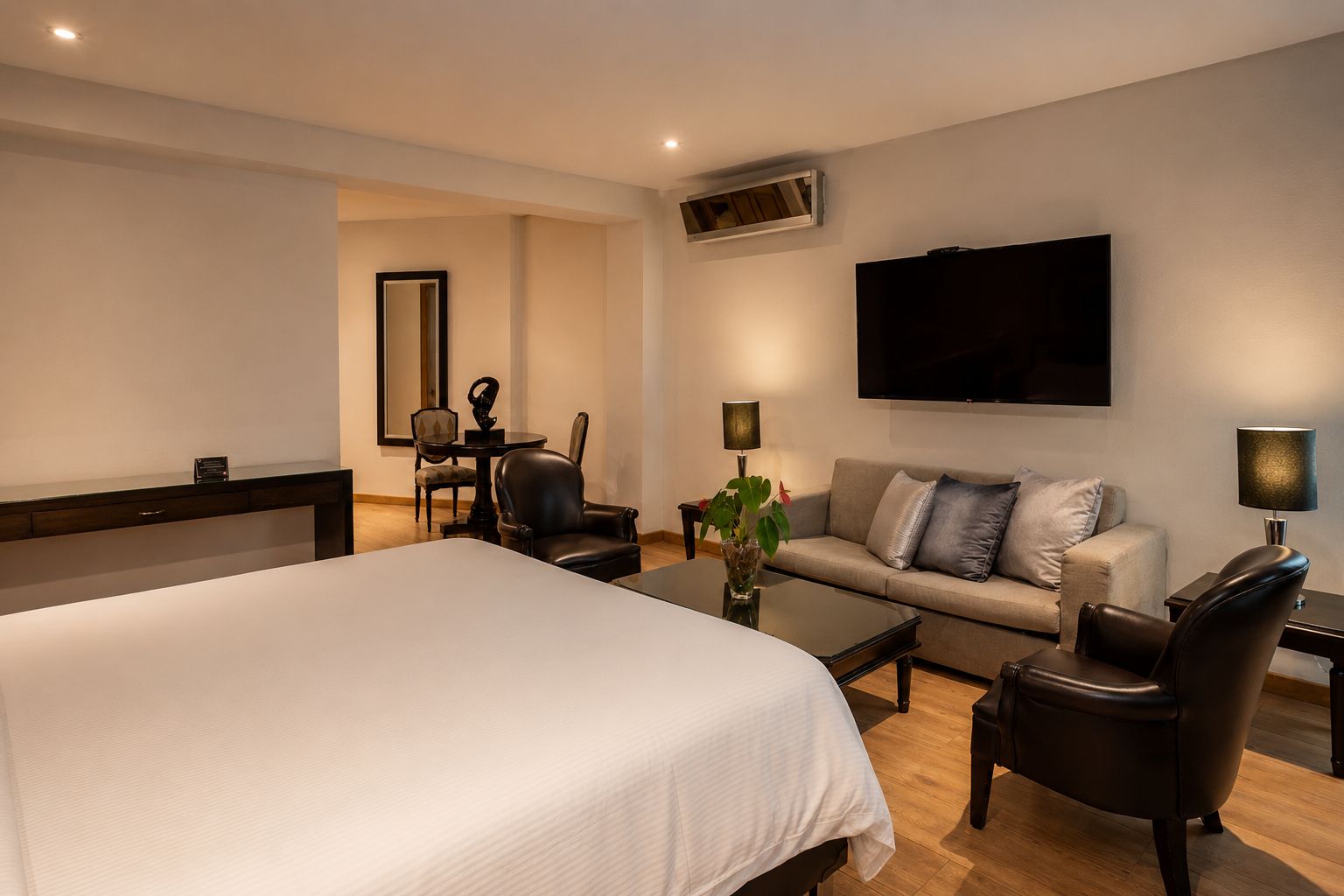 A hotel room with a large bed, a sofa, a coffee table, a TV, and a desk with a chair.