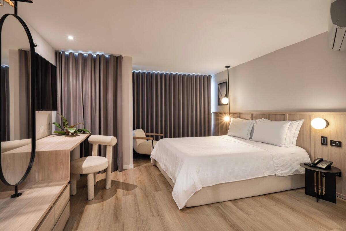 Una habitación de hotel moderna con una cama grande, un escritorio con una silla, una mesita y un espejo.