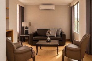 Una sala de estar moderna con un sofá, dos sillones, una mesa de centro, una lámpara y un equipo de aire acondicionado.