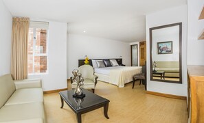 A hotel room with a bed, a sofa, a coffee table, a chair, and a mirror. - Hotel Egina Medellín (Medellín)