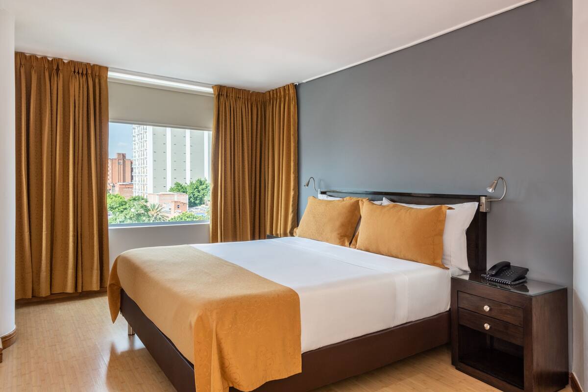 Habitación de hotel con una cama grande, una mesita de noche con teléfono y una ventana con cortinas.