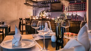 Un ambiente de restaurante con una zona de bar al fondo, que incluye botellas de vino y una pantalla de televisión.