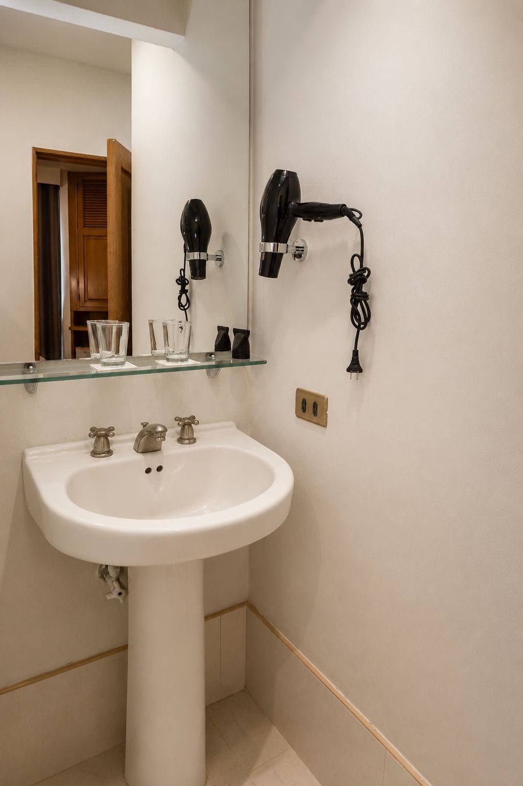 Un baño con un lavabo blanco, un espejo y un secador de pelo montado en la pared.