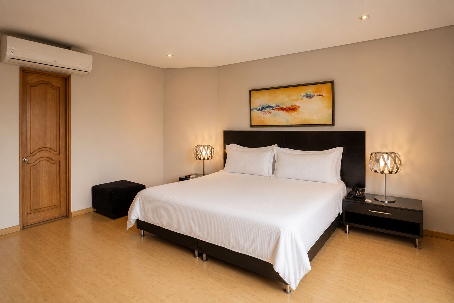 A bedroom with a bed, bedside tables, a nightstand, an air conditioning unit, and a painting on the wall.