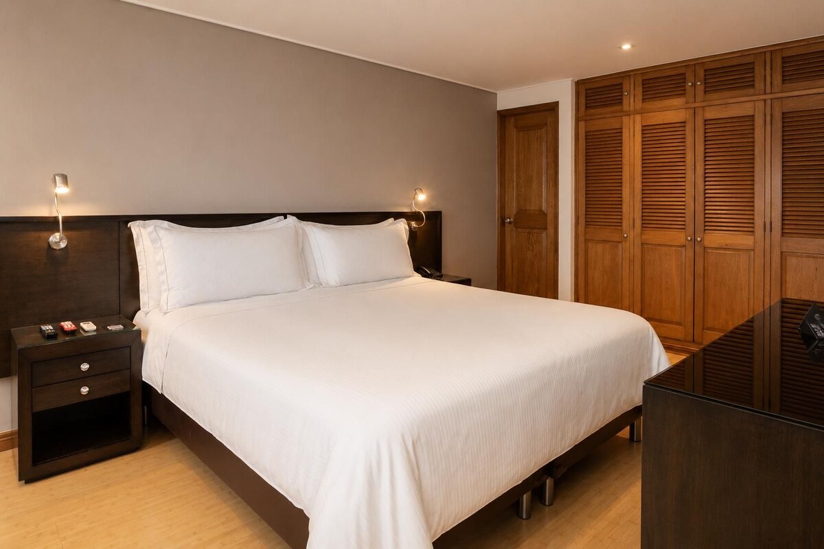 Una habitación de hotel con cama, mesitas de noche, armario y escritorio.