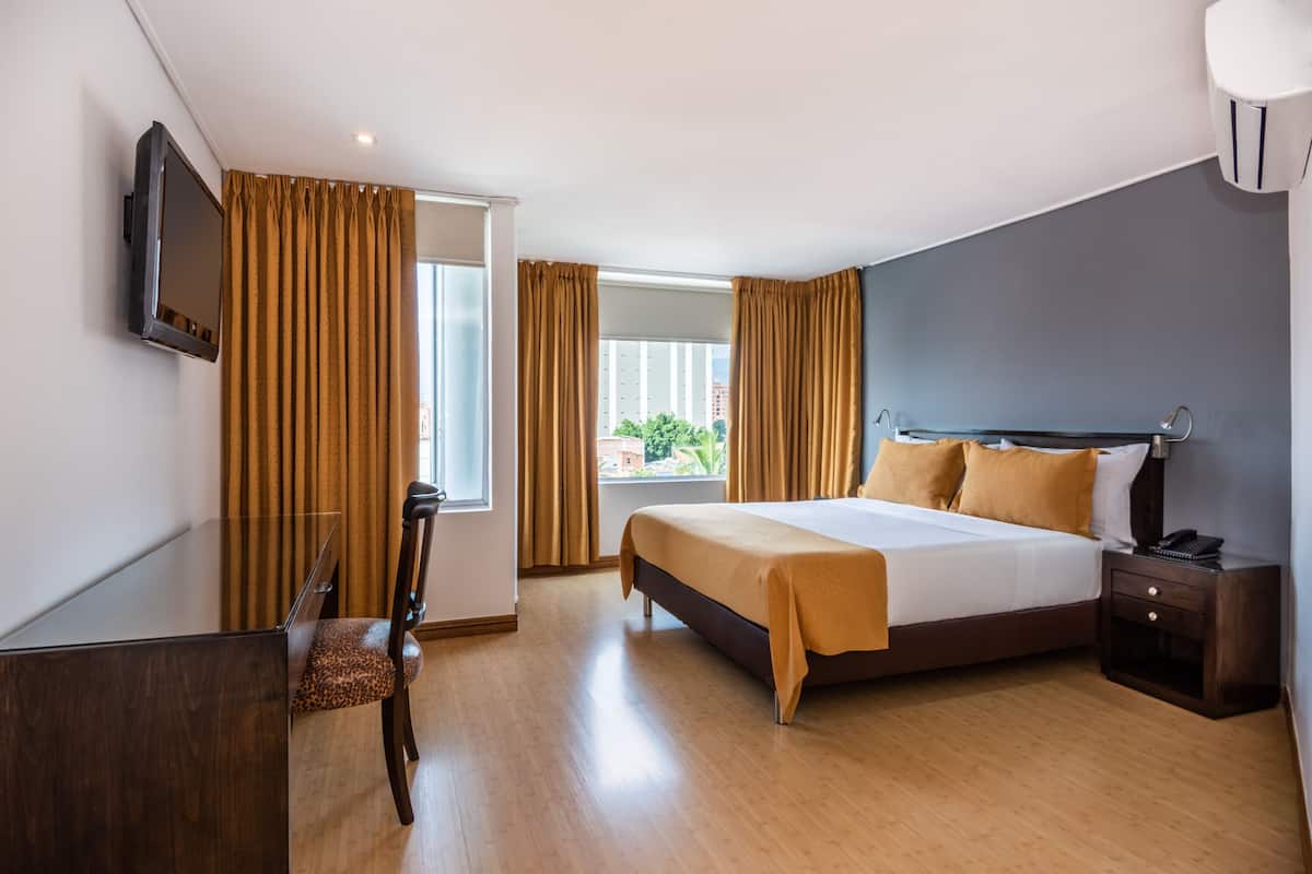 Habitación de hotel con cama, mesita de noche, lámpara, televisor y vistas al exterior.