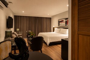 Habitación de hotel con cama, escritorio, silla, televisor y un cuadro en la pared.