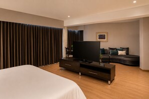 A modern hotel room with a large bed, a flat-screen TV, a dark-colored sofa, and a large window with curtains. - Hotel Egina Medellín (Medellín)