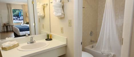 A hotel bathroom with a sink, mirror, towel rack, toilet, and shower.