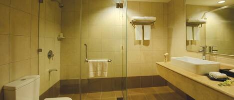 Un baño moderno con ducha envuelta en vidrio, inodoro blanco, lavamanos grande y espejo.