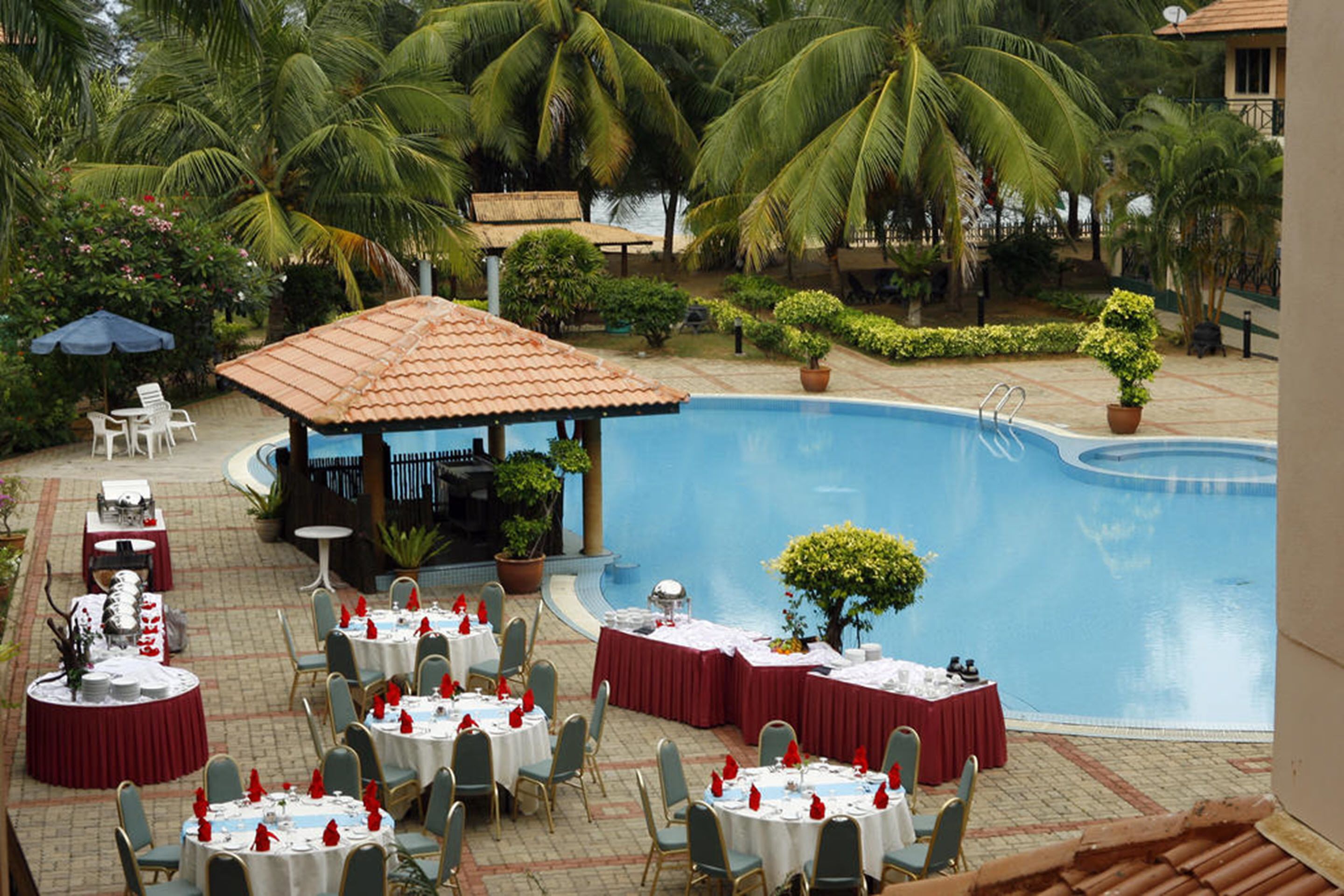Ein Außenbereich zum Essen mit runden Tischen und Stühlen, einem Pool und Palmen.