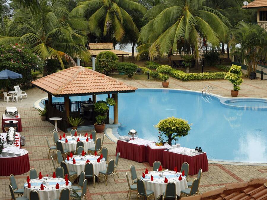 An outdoor dining area with round tables and chairs, a pool, and palm trees.