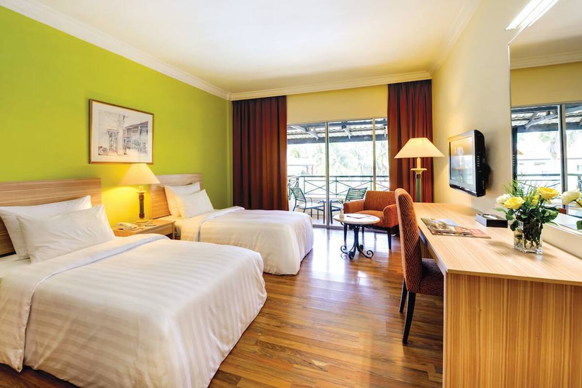 A hotel room with two beds, a desk, a chair, a TV, and a balcony with a table and chairs.