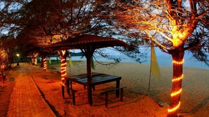 A beachside walkway with a wooden bench and a covered seating area, surrounded by trees wrapped with lights. - The Qamar Paka (Dungun)