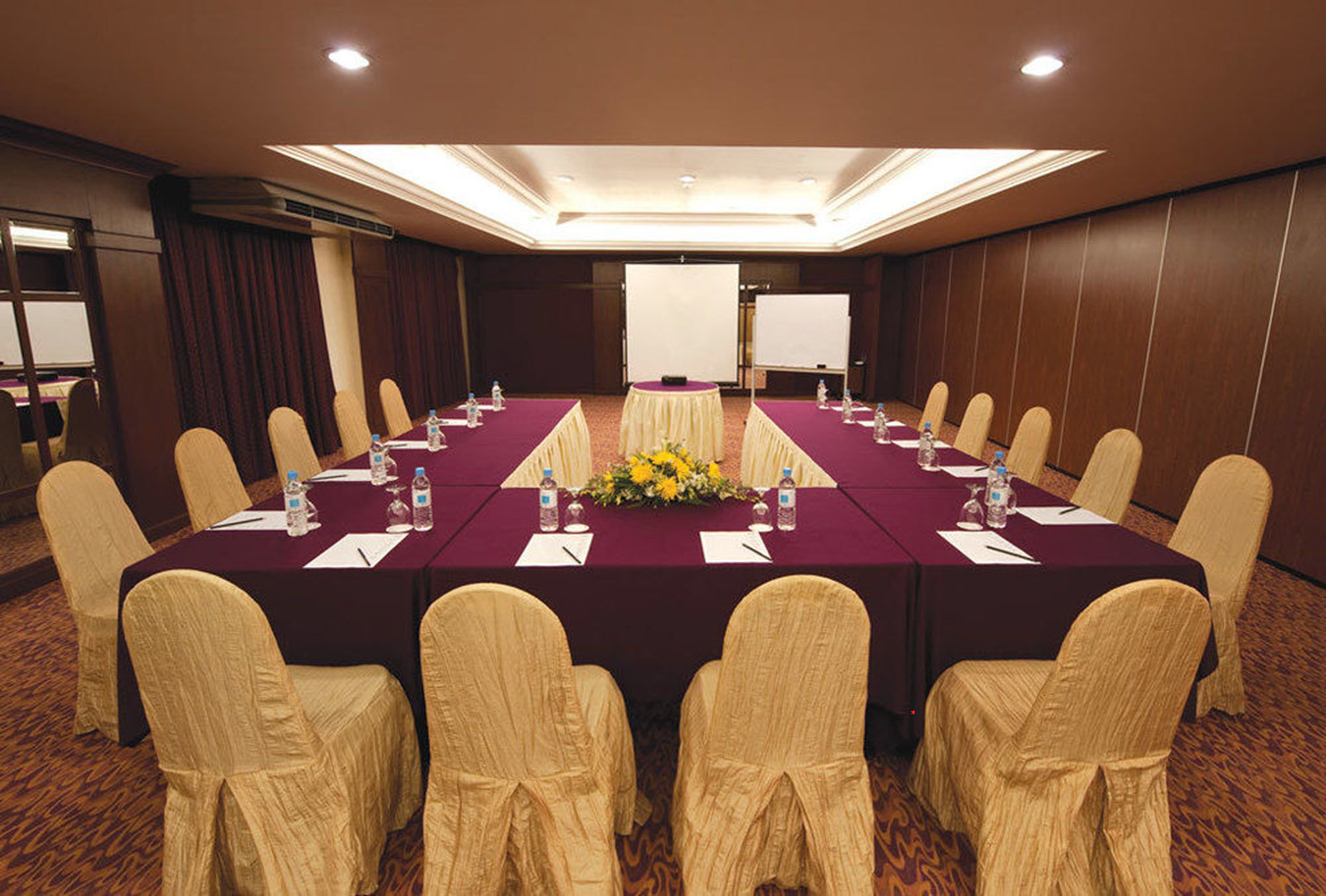 A conference room with a long table, chairs, a projector screen, and a floral centerpiece.