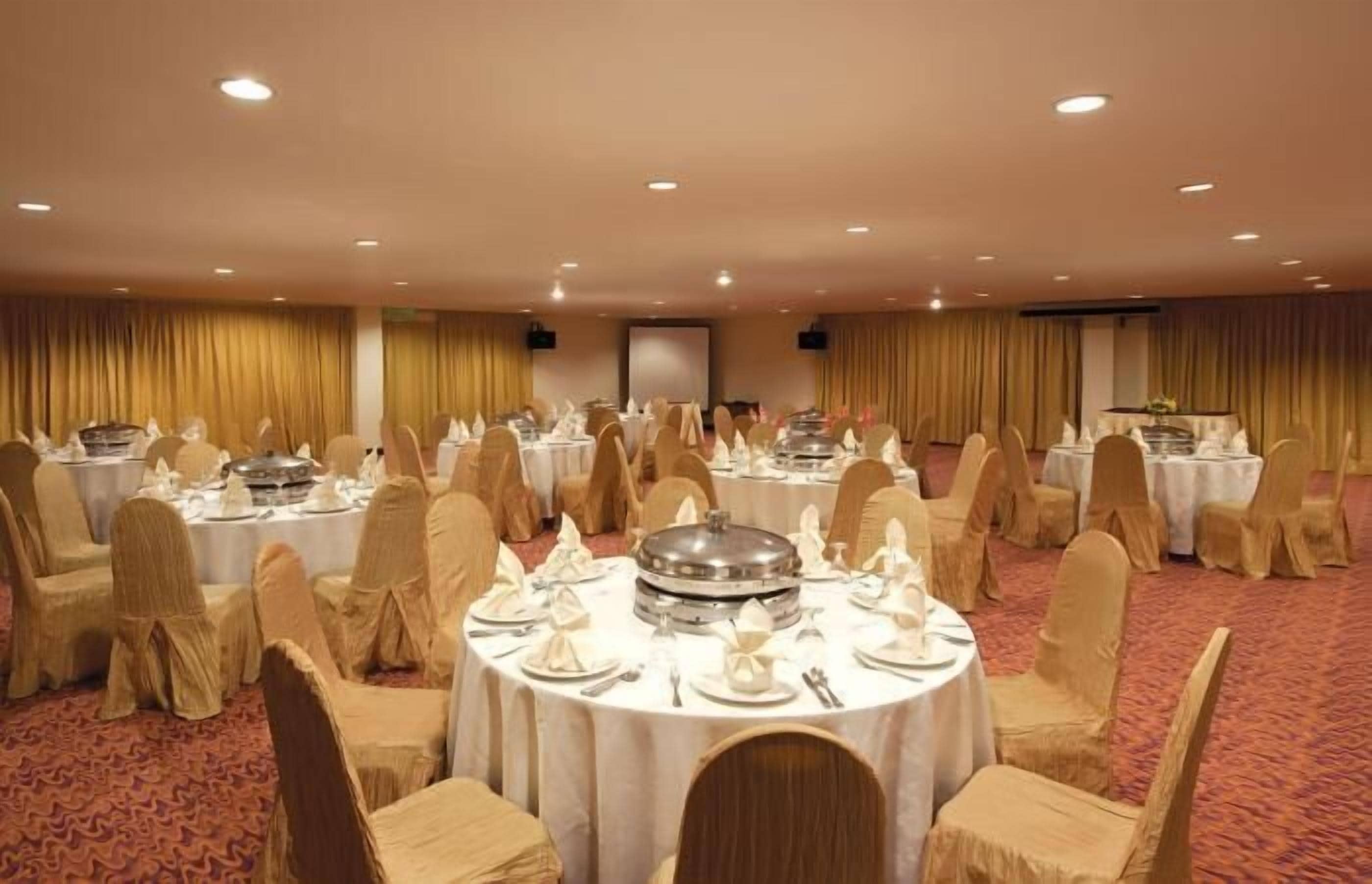 A banquet hall with round tables set for dining, covered chairs, and a stage at the front.