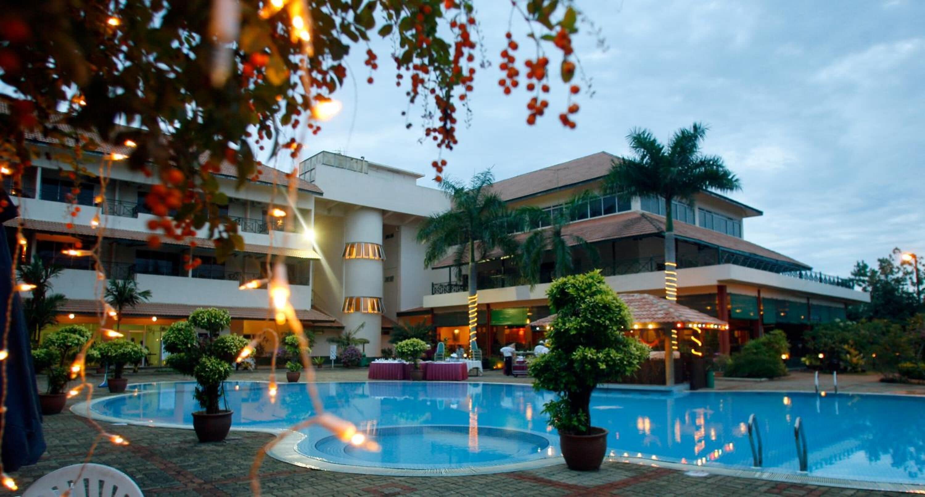 A hotel with a swimming pool, potted plants, and a multi-story building.