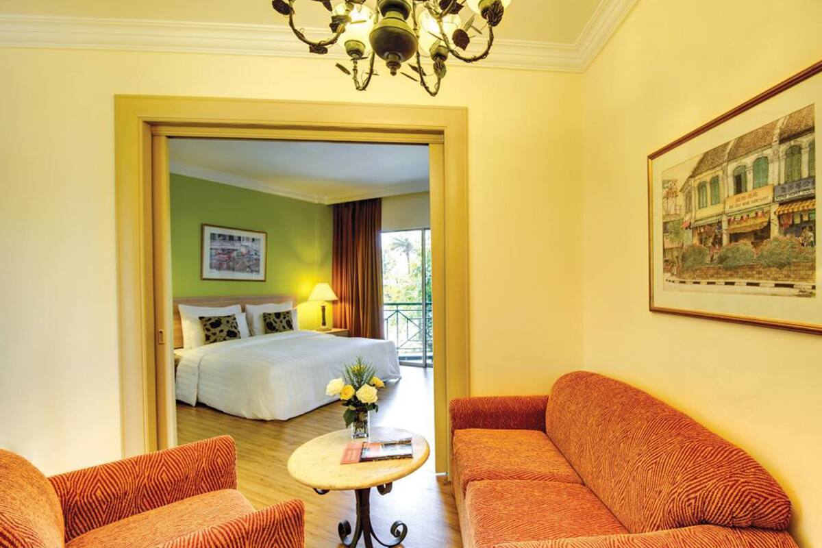 A hotel room with a bed, a sofa, a small table, and a chandelier.
