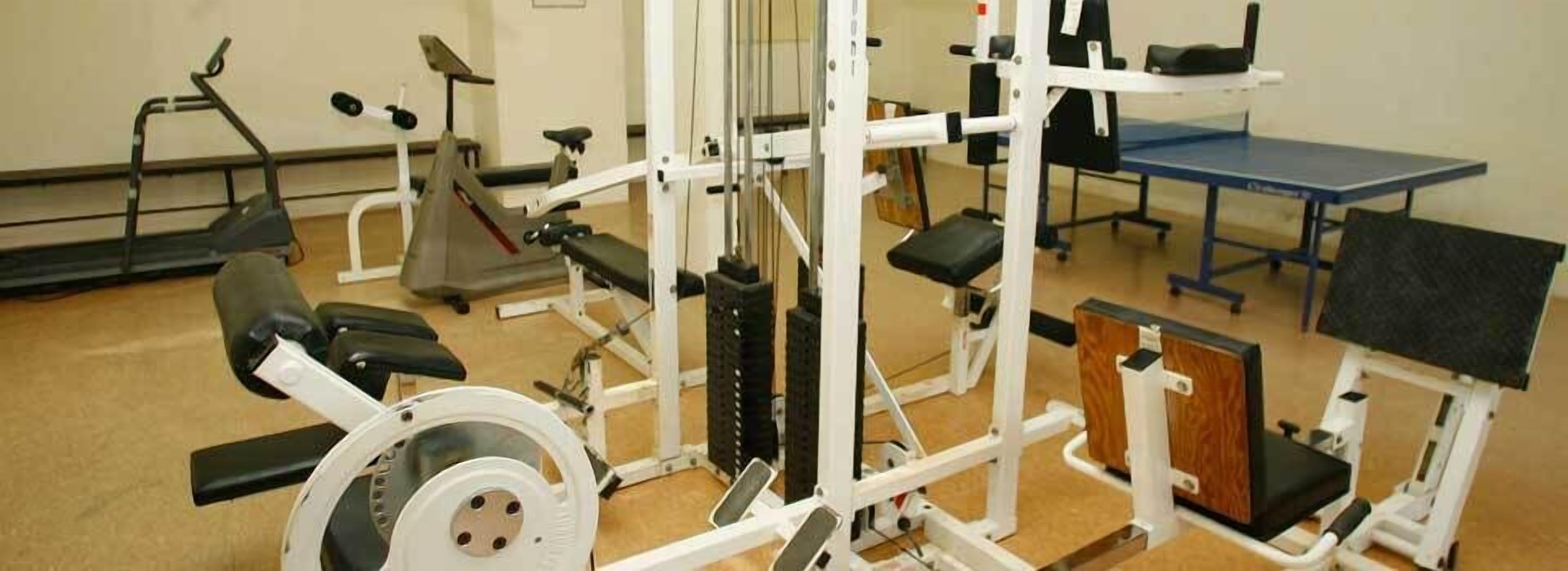 Un gimnasio con diferentes máquinas de ejercicio, incluyendo una cinta de correr, una elíptica y máquinas de pesas.