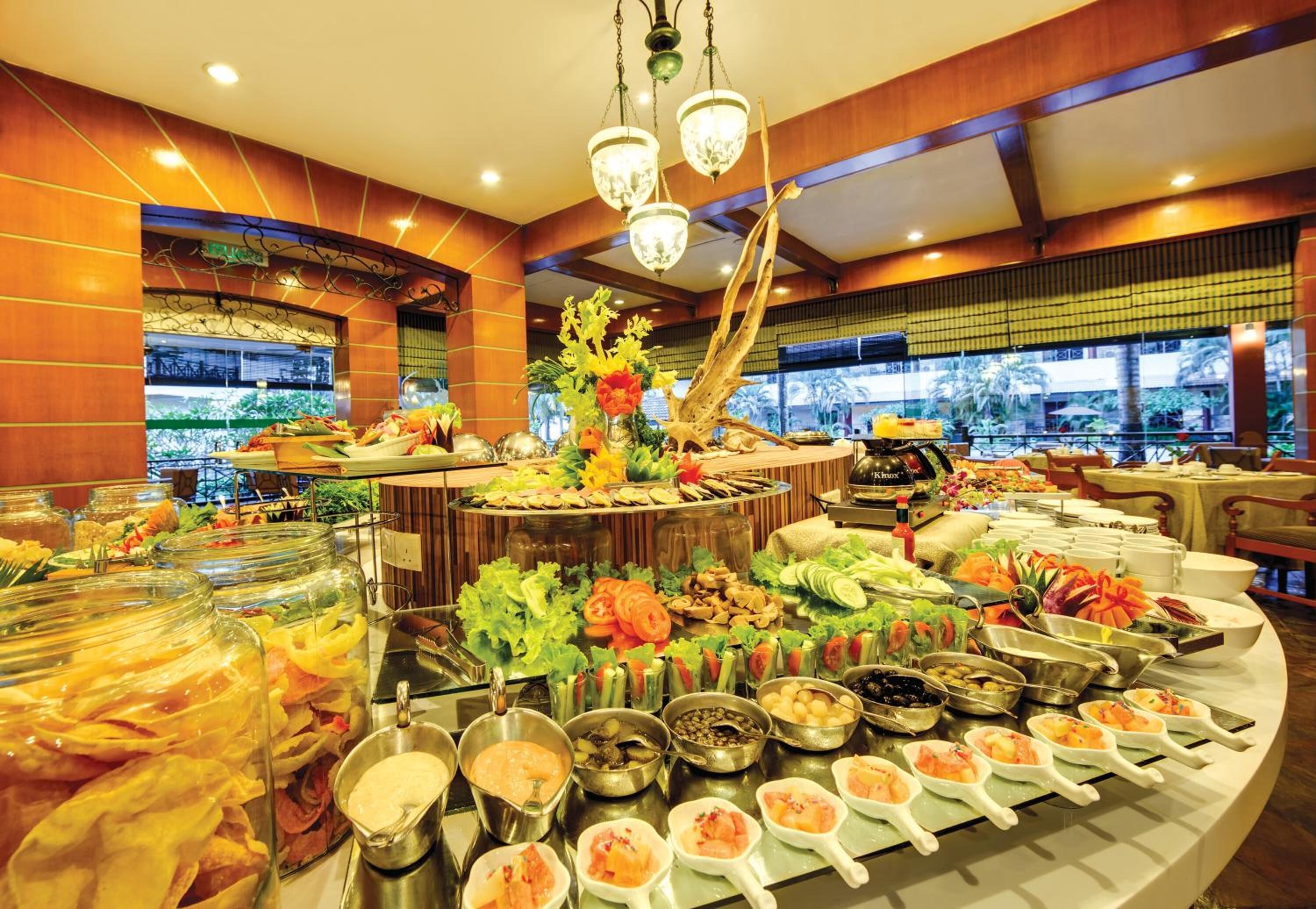 A buffet with various food items, including fruits, vegetables, and meats, arranged on a large table with a decorative centerpiece.