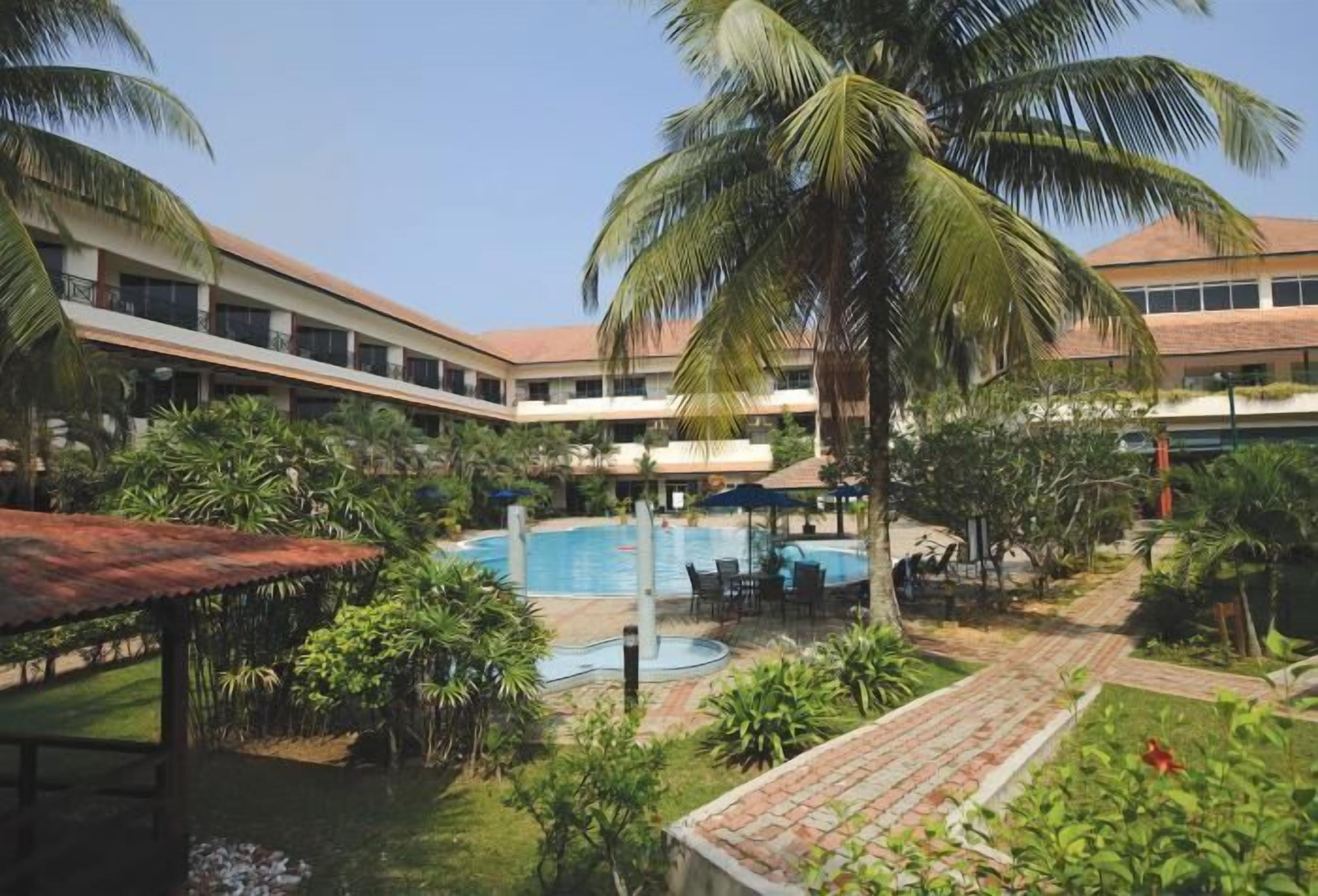A hotel courtyard with a swimming pool, palm trees, and outdoor seating areas.