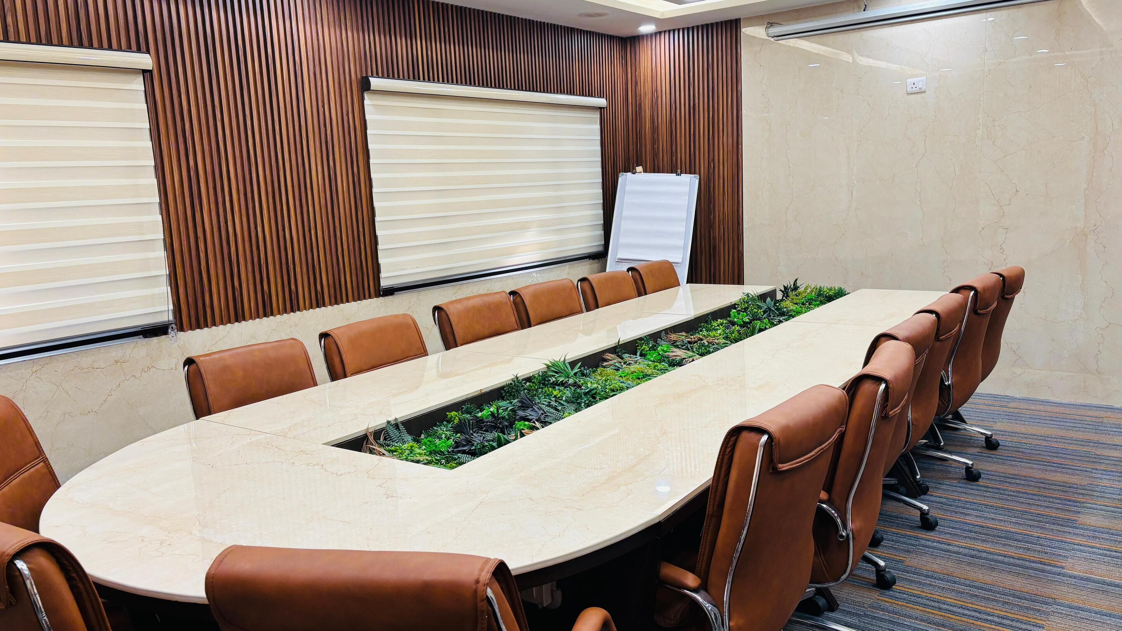 Un salón de conferencias con una larga mesa, sillas de cuero marrón, una pizarra y paneles de madera.