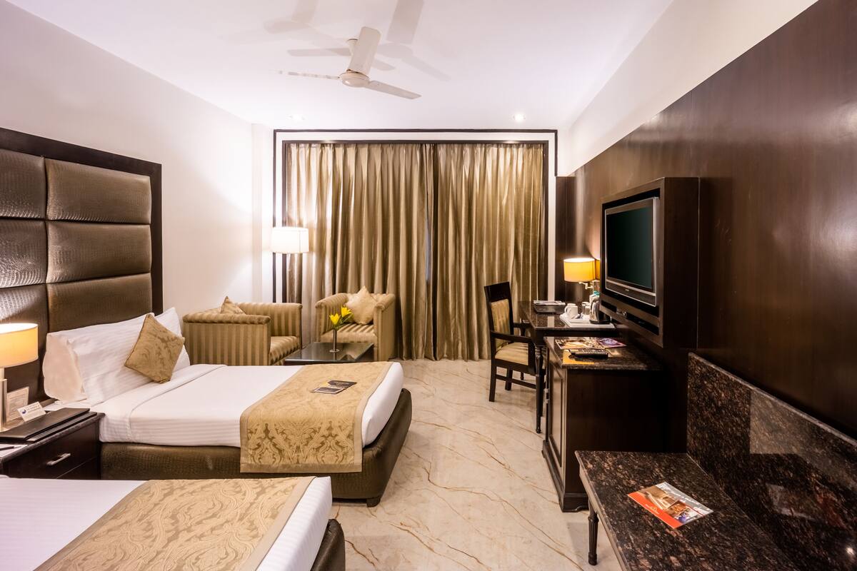 A hotel room with a bed, a desk, a chair, a television, and a ceiling fan.