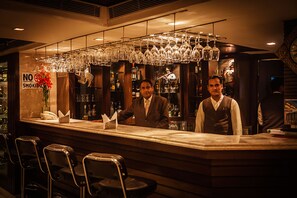 A bar area with two bartenders, a no smoking sign, and a variety of bottles and glasses. - Hotel Shanti Palace (New Delhi)