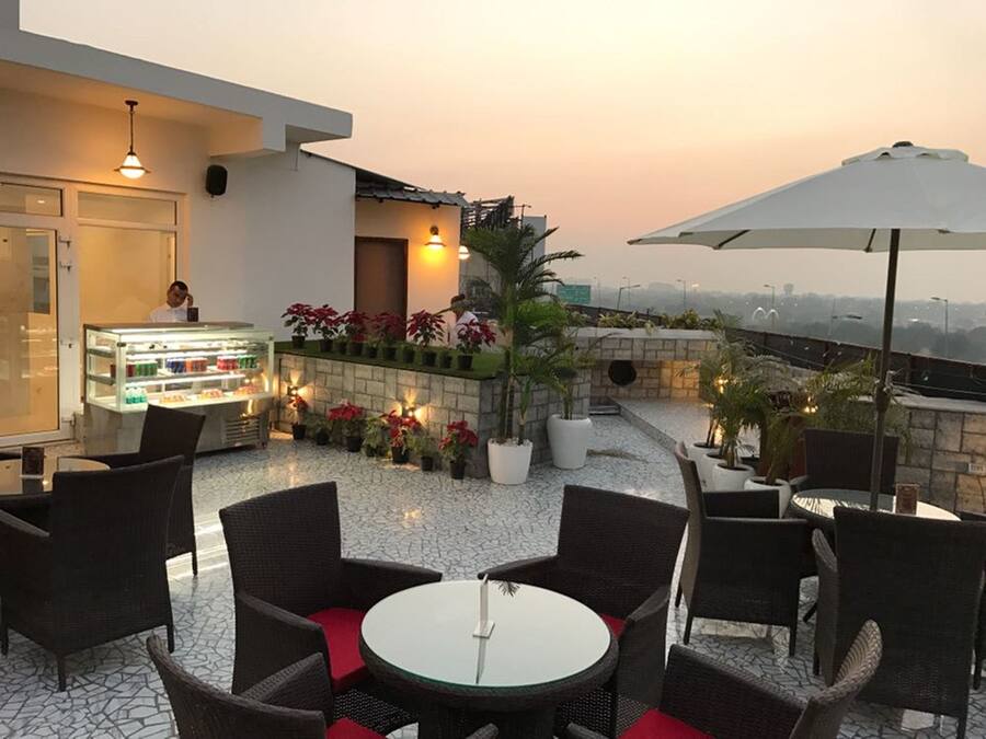 Una terraza en la azotea con mobiliario de mimbre, una vitrina con alimentos, plantas en macetas y vistas panorámicas de la ciudad.
