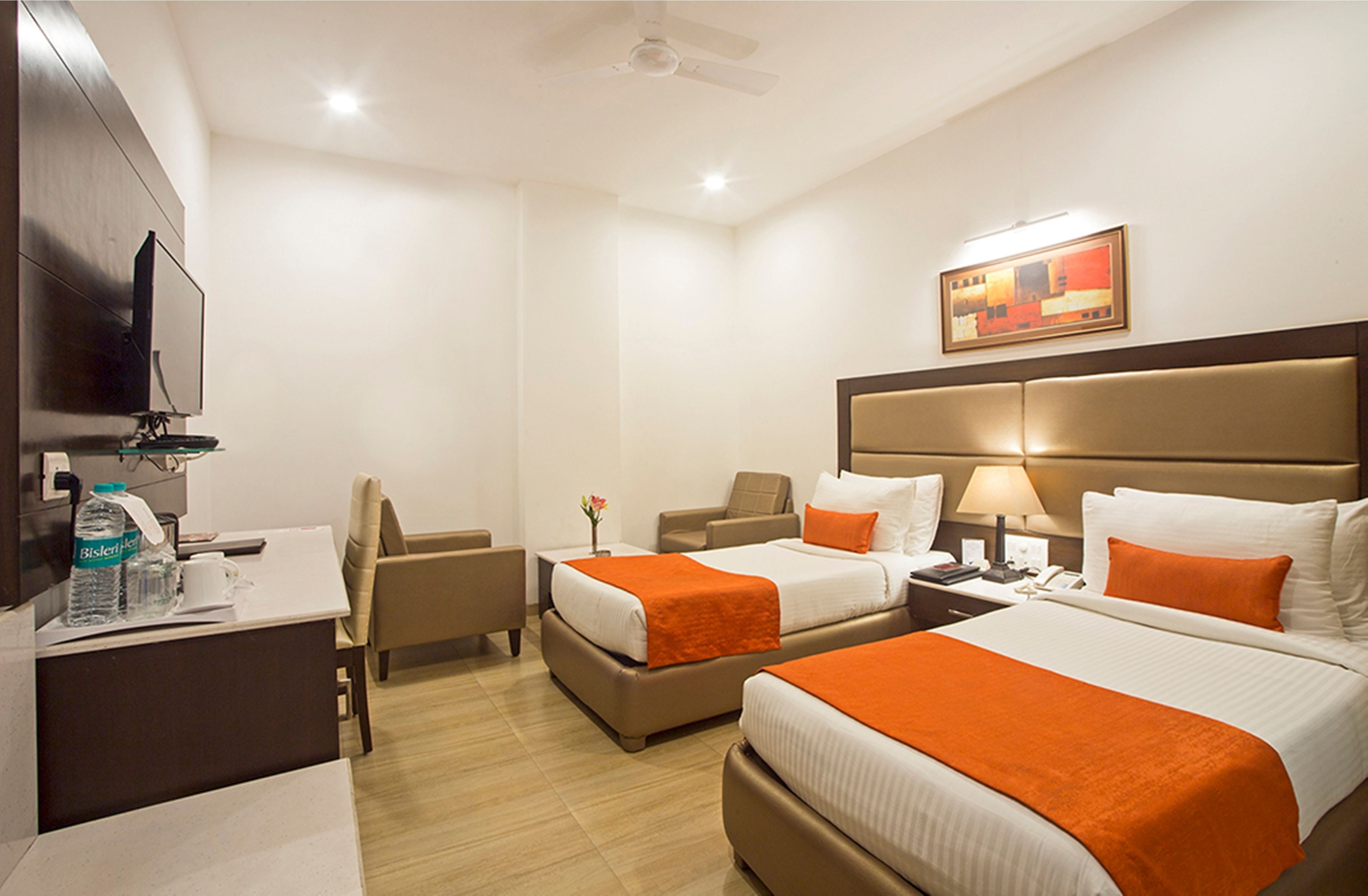 Quarto de hotel com duas camas, uma escrivaninha, uma cadeira, televisão e um quadro na parede.
