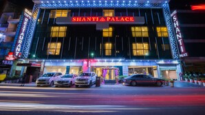 A hotel named Shanti Palace with a modern facade, illuminated signage, and a parking area with several cars. - Hotel Shanti Palace (New Delhi)