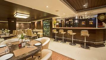Un restaurante con zona de bar, varias mesas con sillas y un reloj en la pared.