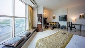 A modern hotel room with a large window, a bed, a sofa, a desk, and a television. - Hotel Shanti Palace (New Delhi)