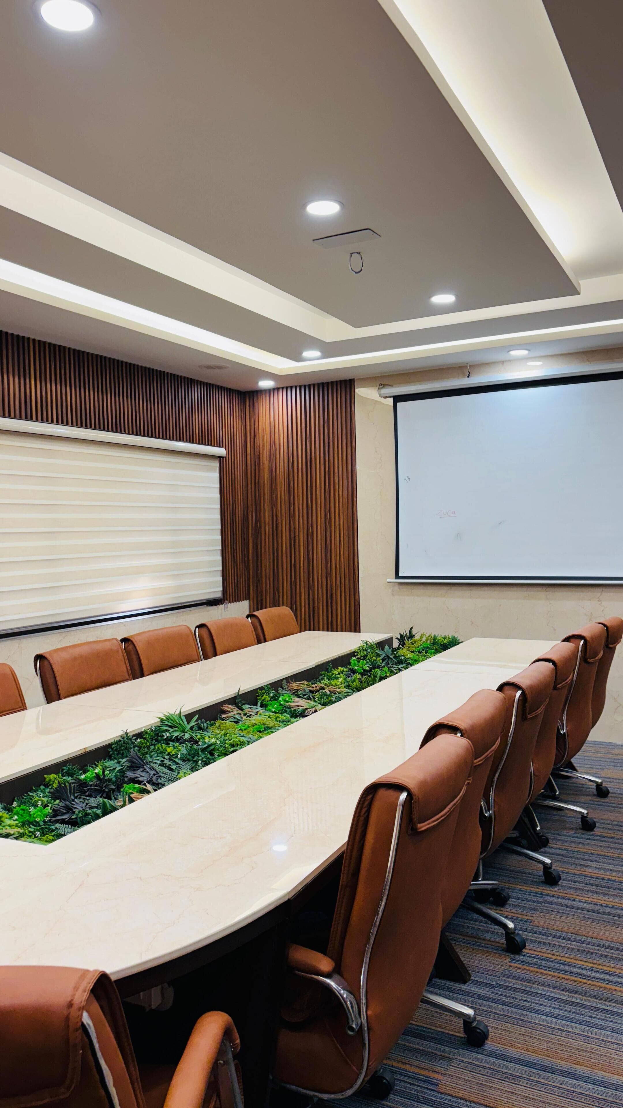 A conference room with a long table, brown leather chairs, a projector screen, and a whiteboard.