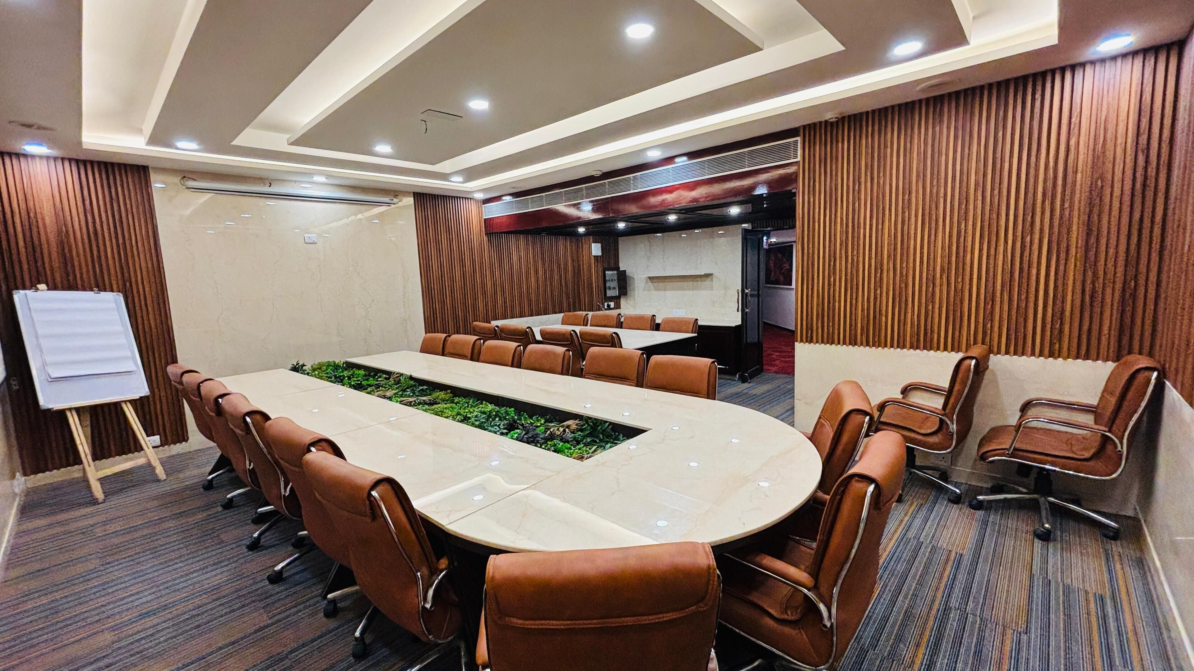 A conference room with a large oval table, brown leather chairs, a whiteboard, and a wooden panel wall.