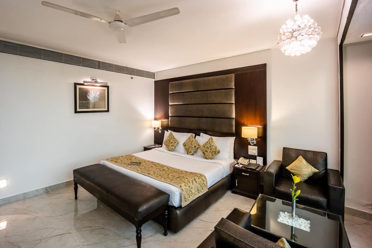 A modern hotel room with a large bed, a desk, a chair, a ceiling fan, and a chandelier.