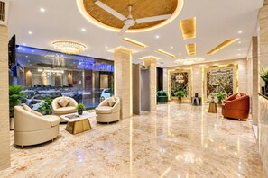 Un vestíbulo de hotel con piso de mármol, asientos de cuero, un ventilador de techo y una mesa de recepción.