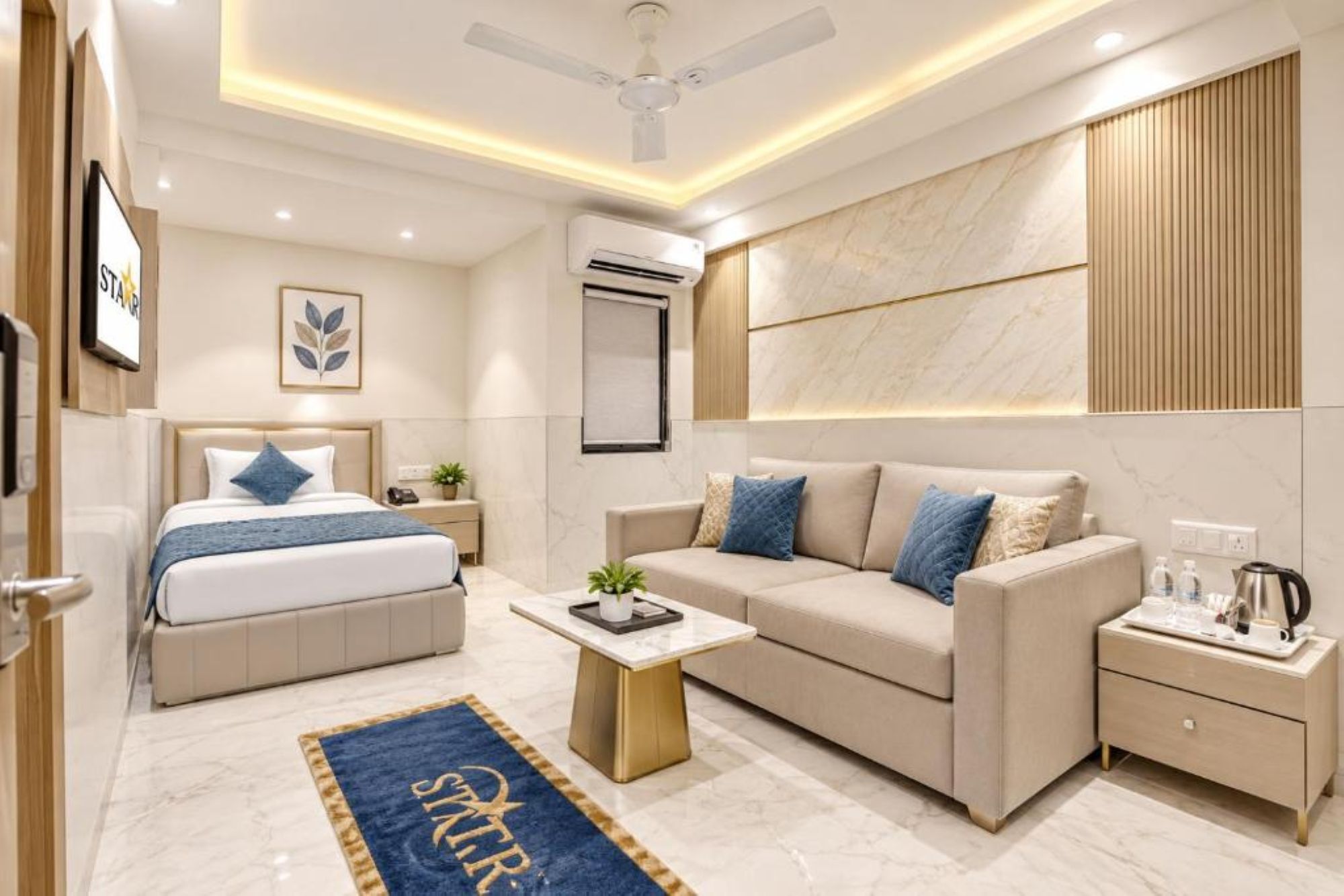 A modern hotel room with a bed, a sofa, a coffee table, and a desk with a kettle.