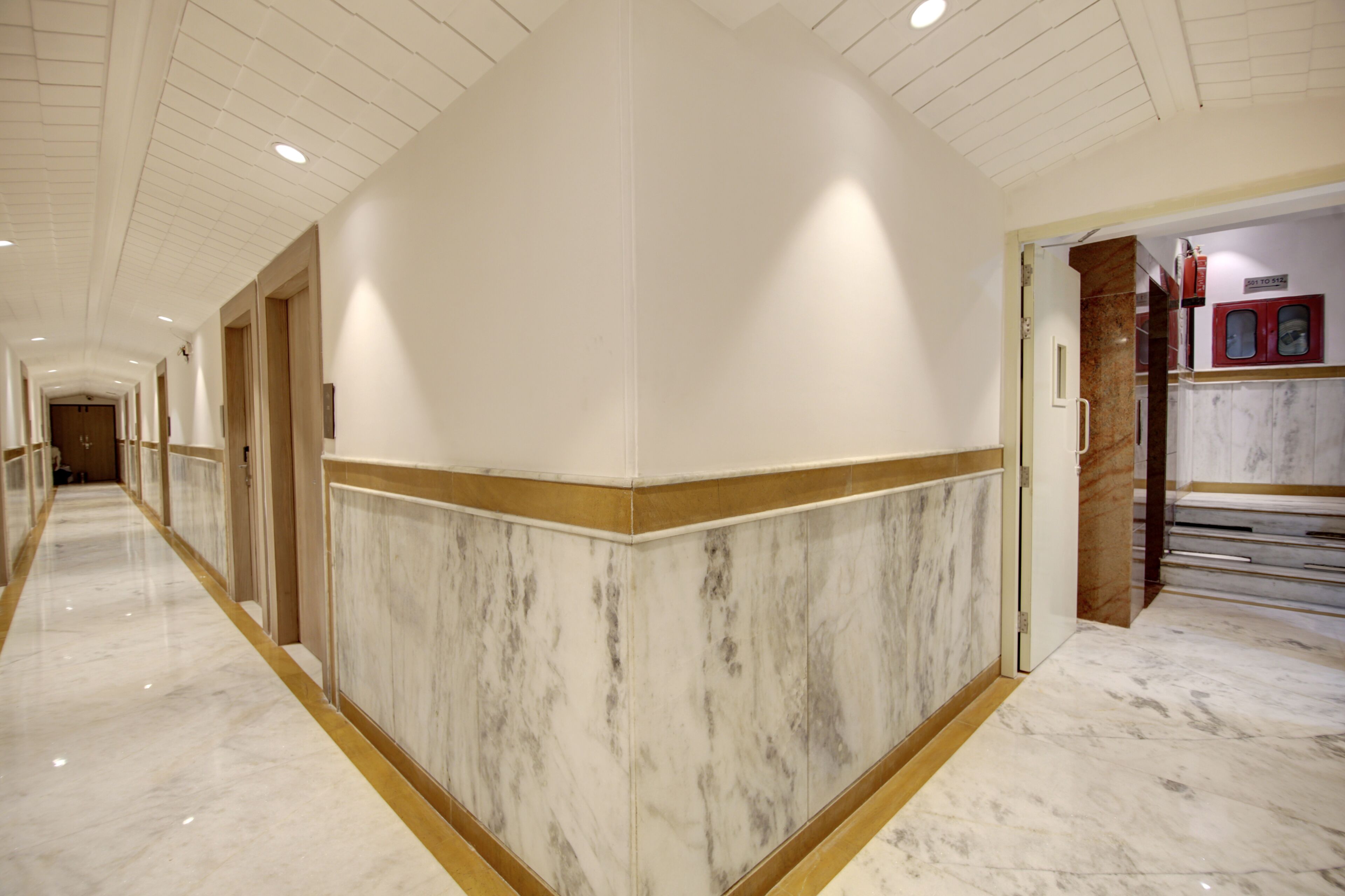 A hallway with marble flooring, a wooden trim, and a door leading to a room with a marble wall and a small window.