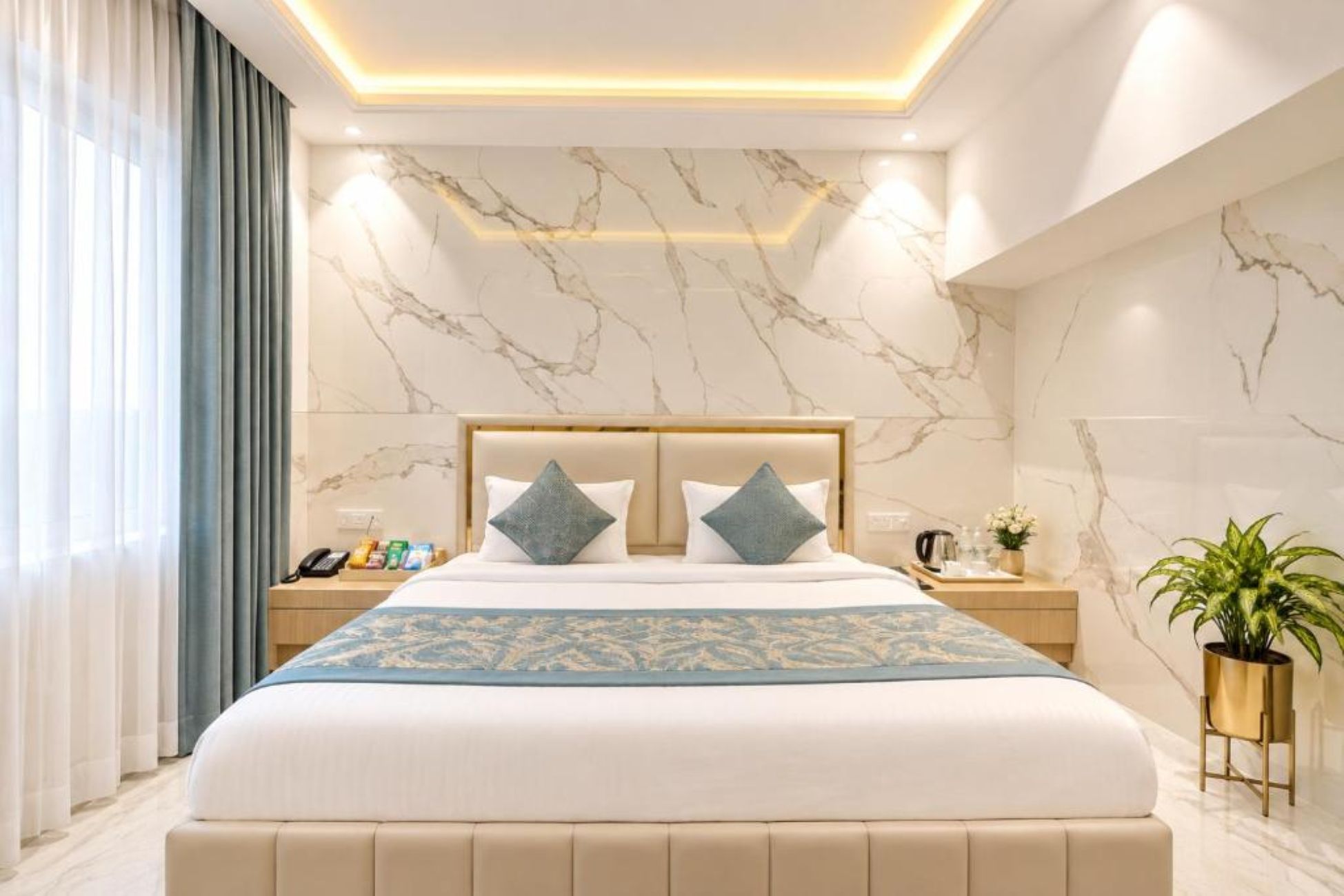 A modern hotel room with a marble-patterned wall, a large bed with a headboard, two bedside tables with lamps, and a potted plant.
