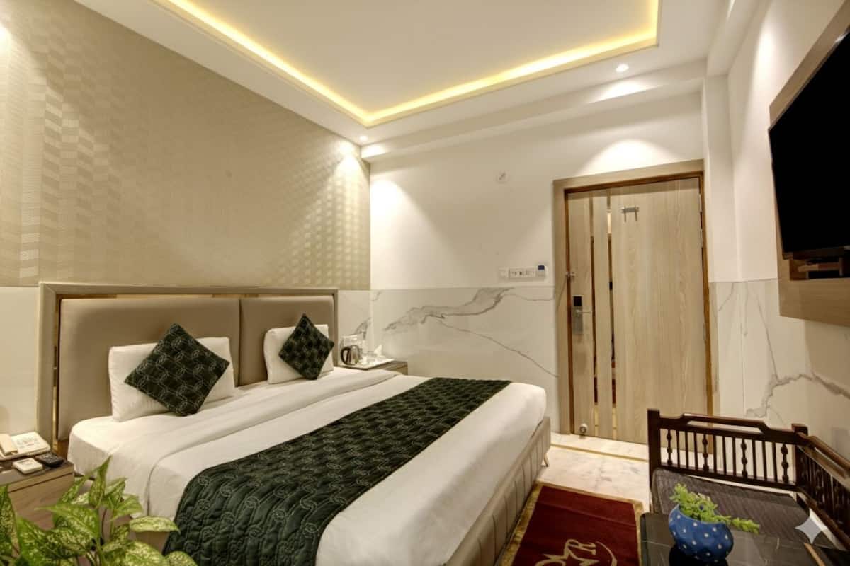 A modern hotel room with a large bed, a desk with a chair, a TV, and a door.